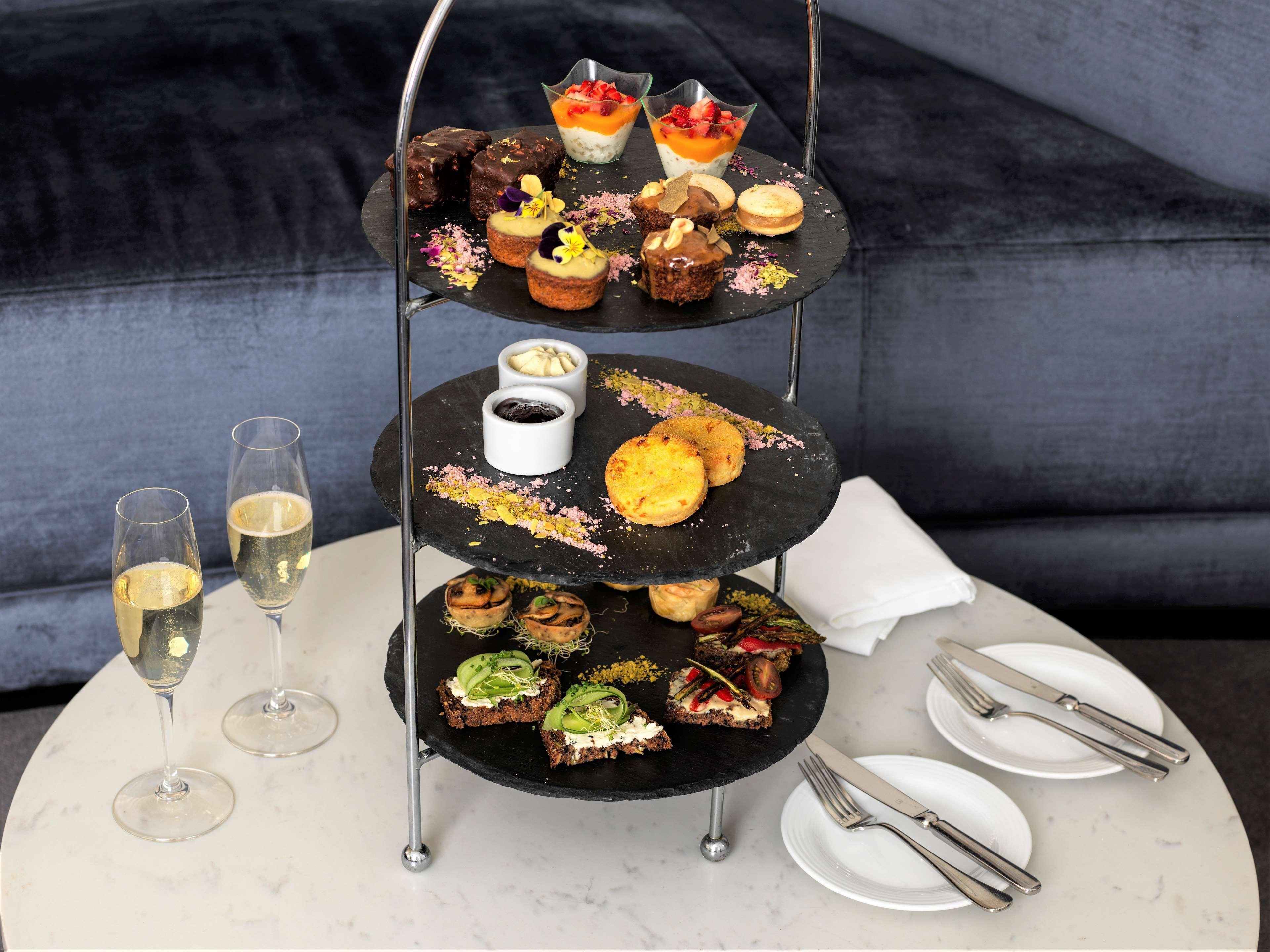 Radisson Blu Plaza Hotel ซิดนีย์ ภายนอก รูปภาพ The photo depicts a tiered serving stand filled with various desserts and snacks. The stand has three levels:

1. **Top Tier**: Features a selection of small desserts, including colorful cups of fruit, cakes, and pastries.
   
2. **Middle Tier**: Con