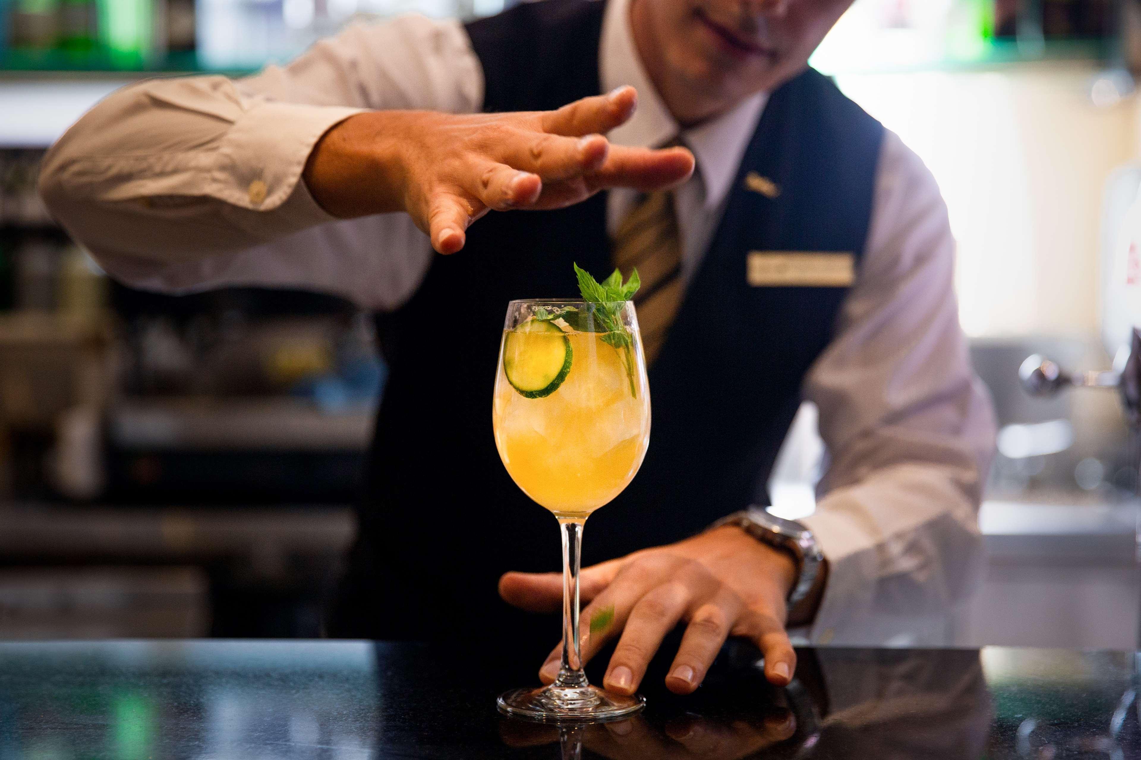 Radisson Blu Plaza Hotel ซิดนีย์ ภายนอก รูปภาพ The photo shows a bartender preparing a cocktail. The bartender is dressed in a formal outfit, featuring a vest and a shirt. He is in the process of presenting a colorful drink in a tall glass, which appears to be garnished with a mint sprig and a sl