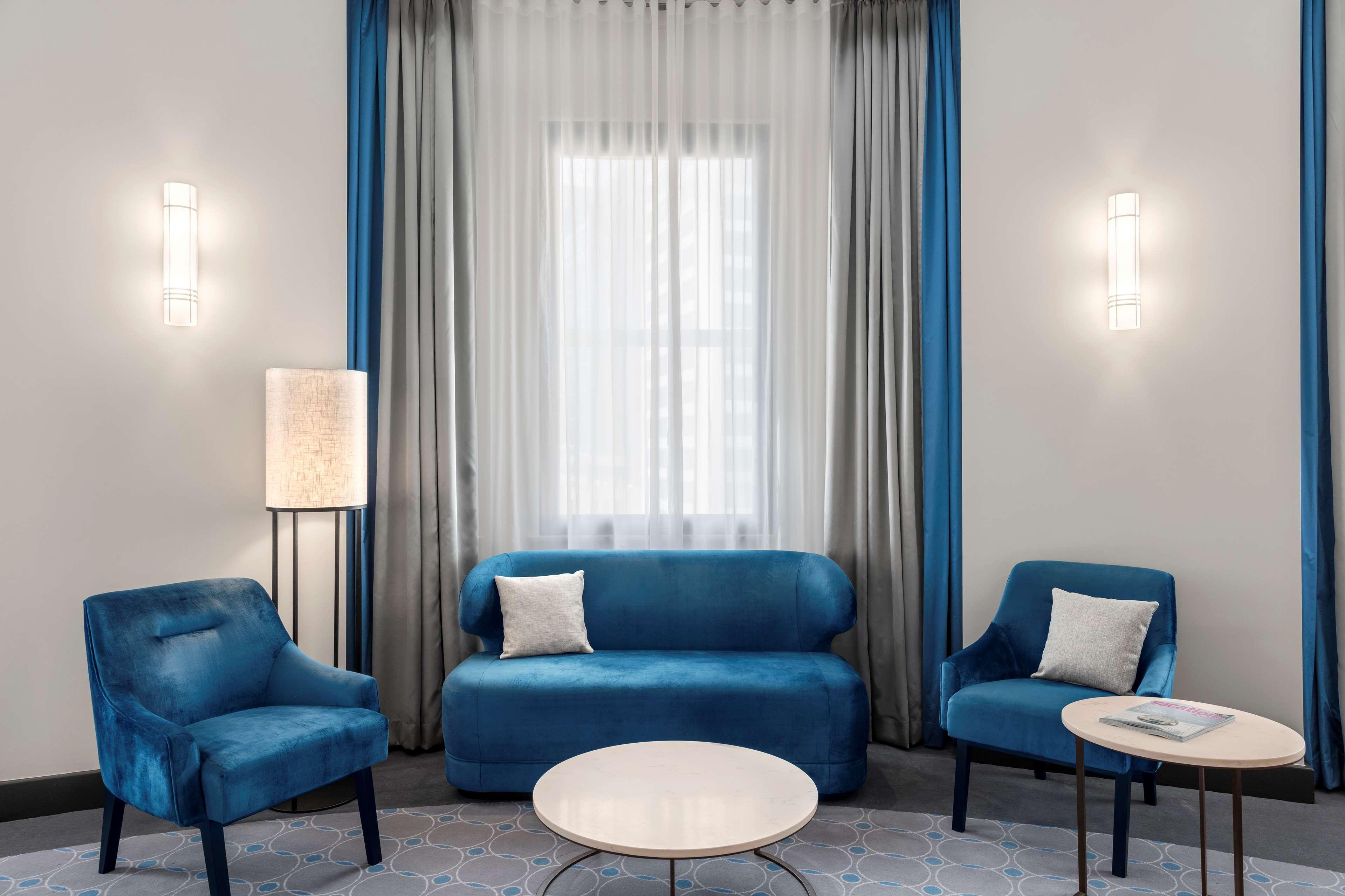 Radisson Blu Plaza Hotel ซิดนีย์ ภายนอก รูปภาพ The photo depicts a modern living space featuring a blue color scheme. There is a blue sofa with a couple of decorative pillows, accompanied by two matching blue armchairs. A round coffee table sits in the center of the seating area. The backdrop inc