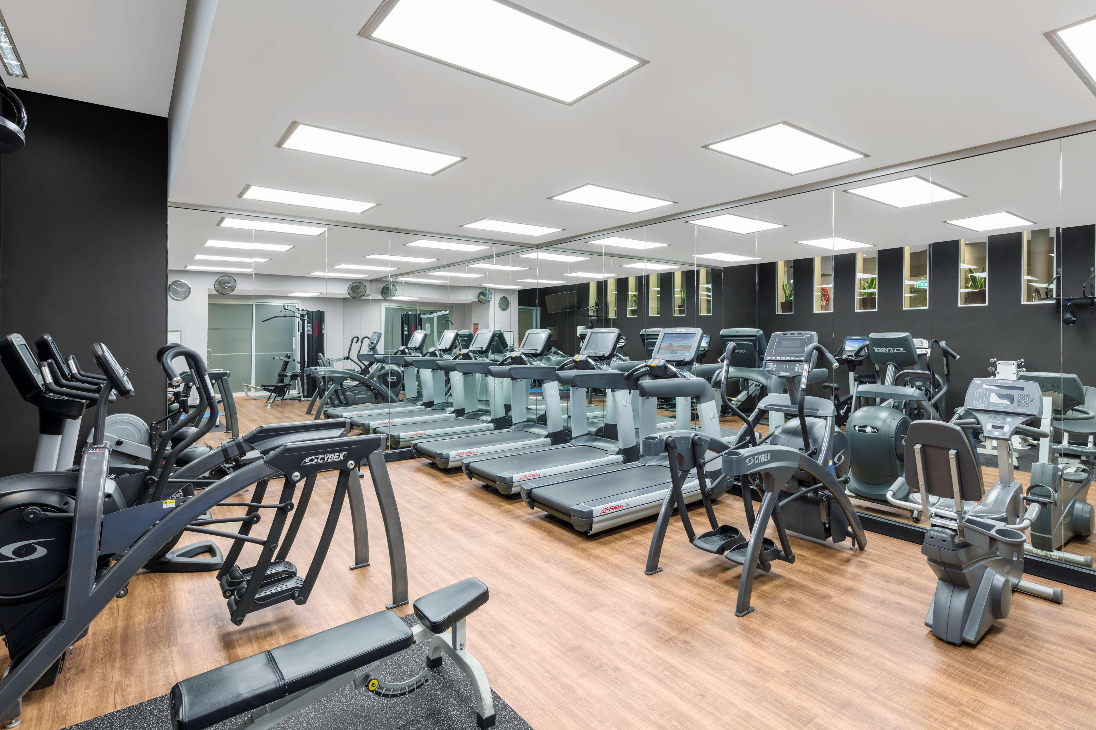 Radisson Blu Plaza Hotel ซิดนีย์ ภายนอก รูปภาพ The photo shows a modern gym interior. It features various exercise machines, including several treadmills and some strength-training equipment. The flooring is wooden, which gives the space a warm feel, and the walls are painted dark, contrasting wi