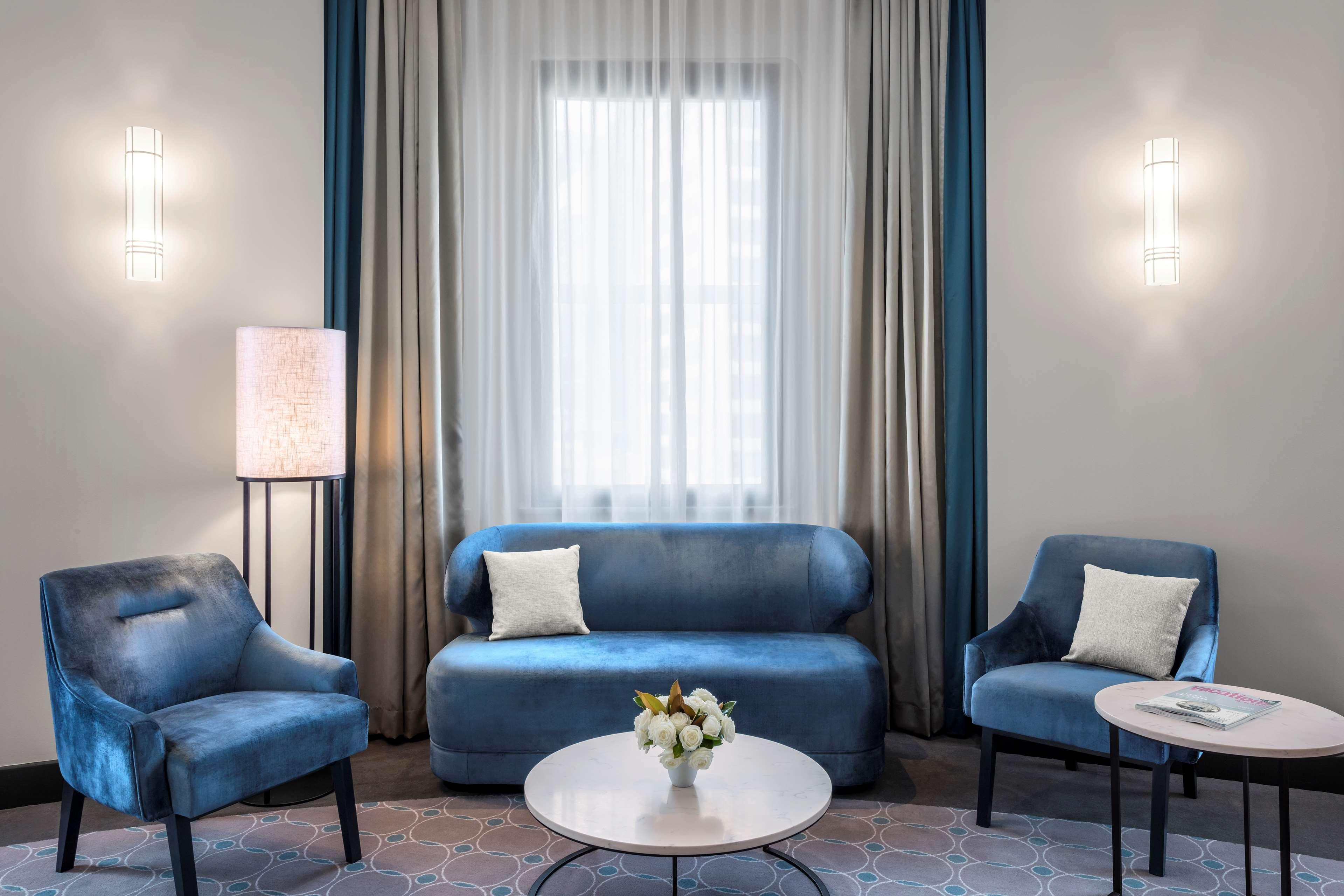 Radisson Blu Plaza Hotel ซิดนีย์ ภายนอก รูปภาพ The photo depicts a stylish and modern living space. It features a light-colored room with soft, neutral walls. There are three pieces of upholstered furniture in a blue hue: a curved sofa and two matching armchairs, each with a white cushion. 

In f
