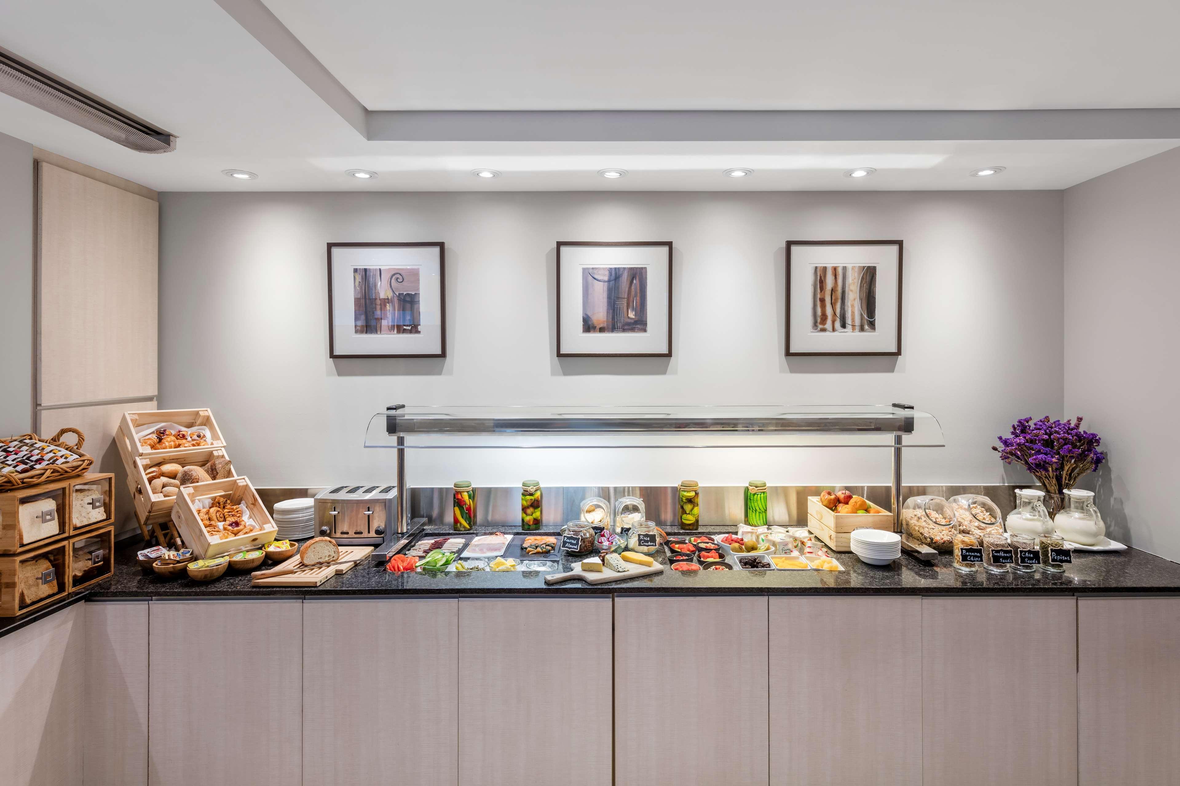 Radisson Blu Plaza Hotel ซิดนีย์ ภายนอก รูปภาพ The photo shows a modern buffet setup. There is a long counter with a sleek surface, displaying a variety of food items. The decor includes neatly arranged canisters, trays, and containers filled with different types of food. These includes bread, pa