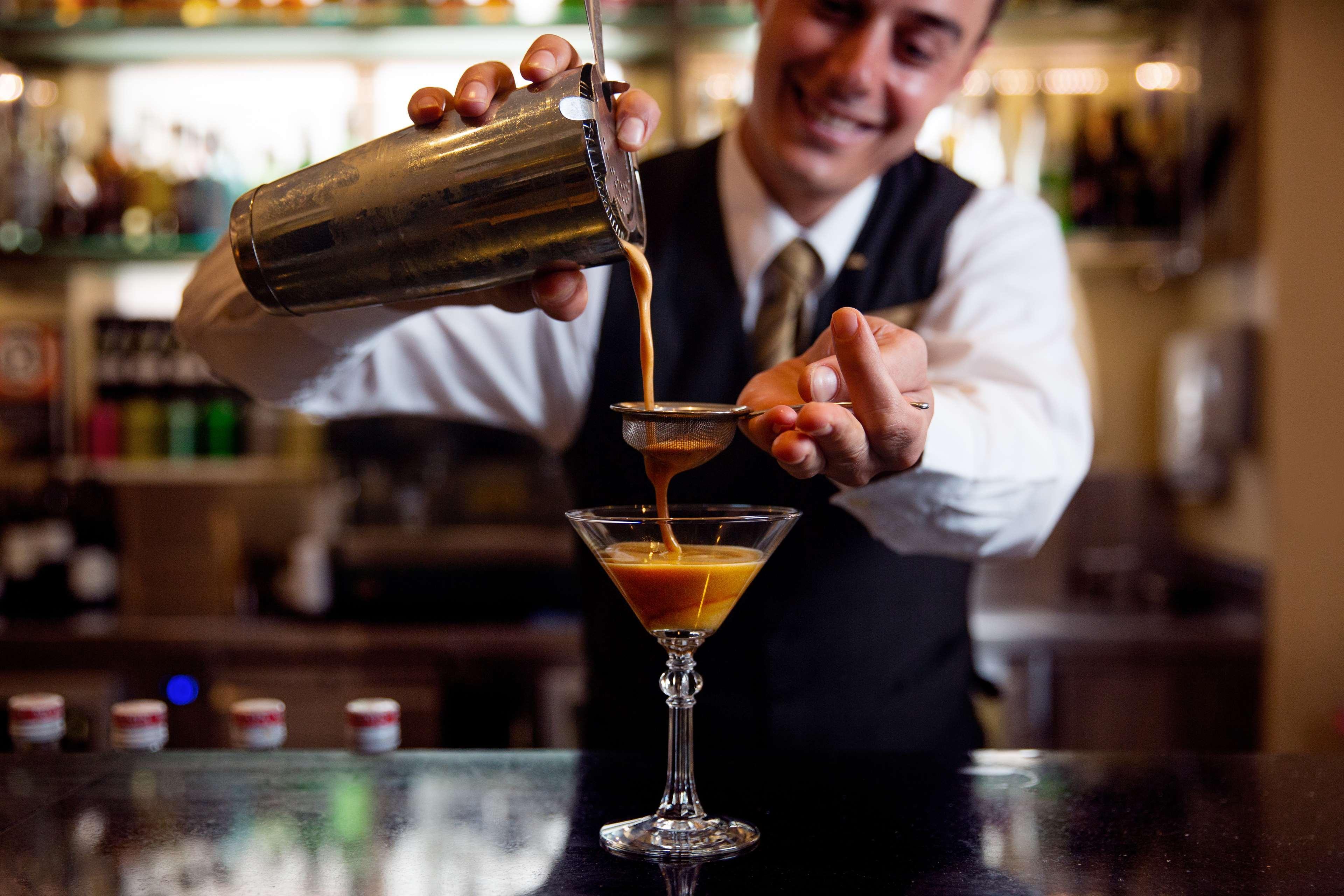 Radisson Blu Plaza Hotel ซิดนีย์ ภายนอก รูปภาพ The photo shows a bartender in a formal outfit, including a vest and tie, skillfully pouring a drink from a cocktail shaker into a martini glass. He is using a strainer to ensure the liquid flows smoothly into the glass, which is placed on a bar coun