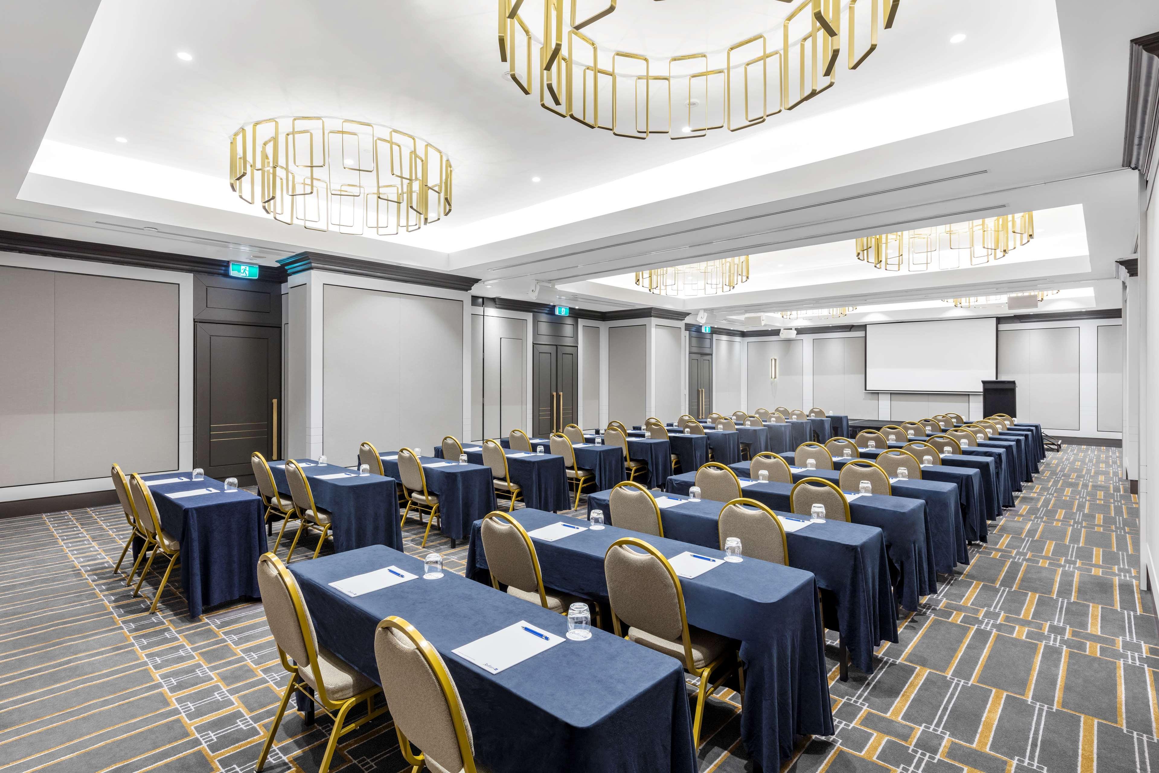 Radisson Blu Plaza Hotel ซิดนีย์ ภายนอก รูปภาพ The photo shows a conference room set up for a meeting or seminar. The room features rows of tables covered with dark blue tablecloths and gold-accented chairs. Each table has a piece of paper and a glass of water placed on it. The lighting is modern