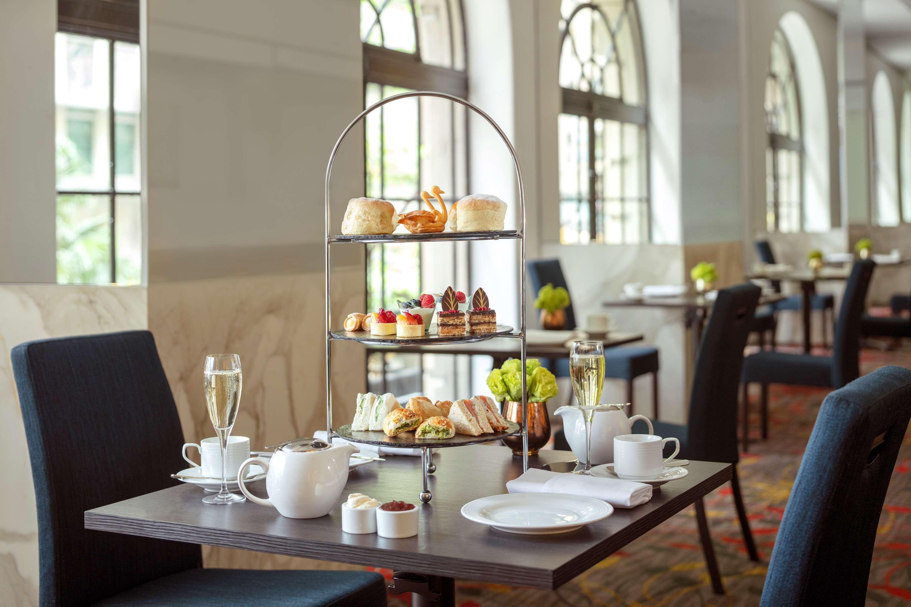 Radisson Blu Plaza Hotel ซิดนีย์ ภายนอก รูปภาพ The photo depicts a beautifully arranged afternoon tea setup on a table in a cozy dining area. In the center, there is a three-tiered stand displaying a variety of treats, including pastries, scones, and finger sandwiches. The table has a teapot, tea