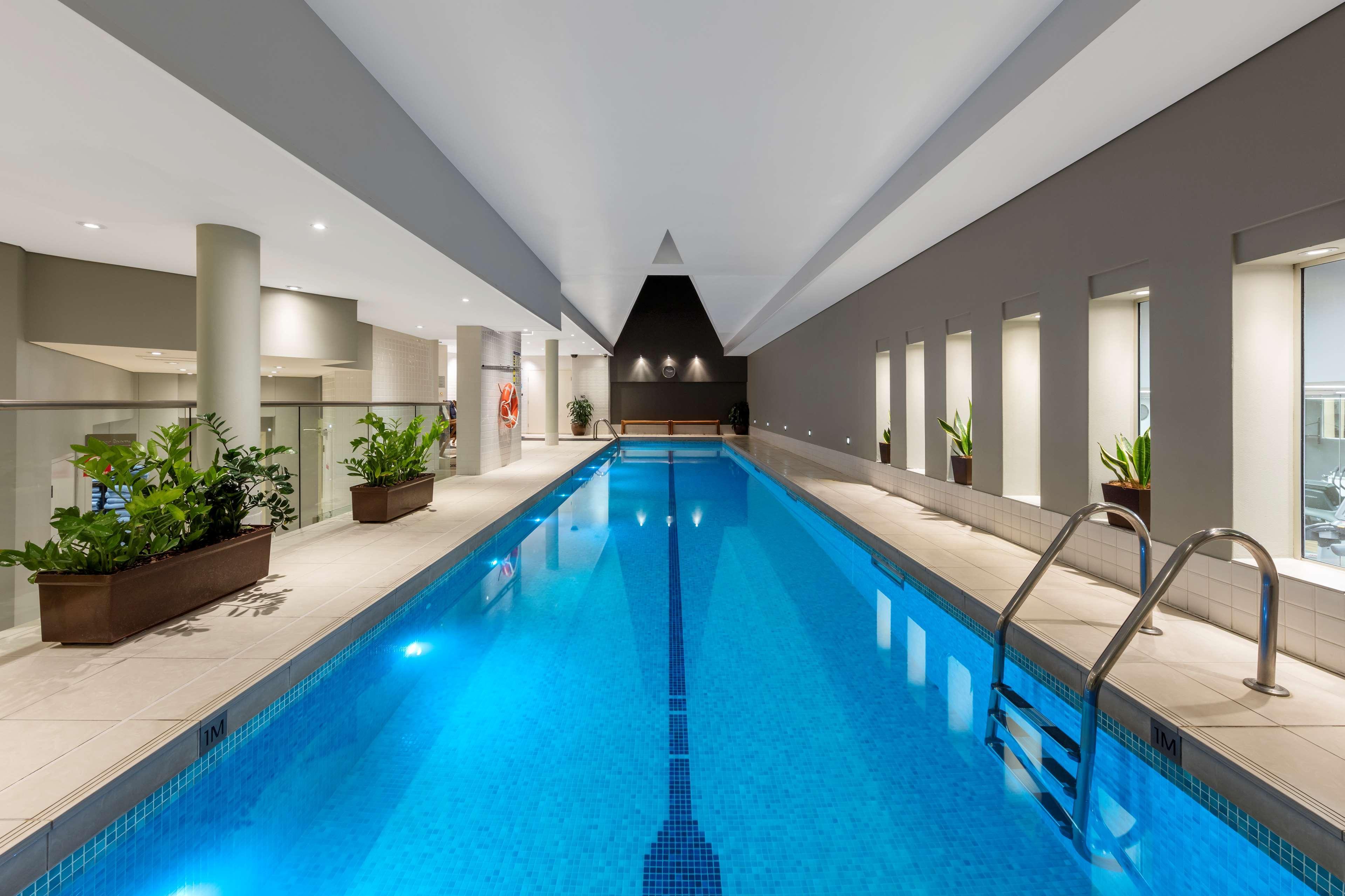 Radisson Blu Plaza Hotel ซิดนีย์ ภายนอก รูปภาพ The photo depicts an indoor swimming pool. The pool is rectangular and features a clean, bright blue surface, with steps leading into it. Surrounding the pool are modern architectural elements, including tall, light-colored walls and a ceiling with a