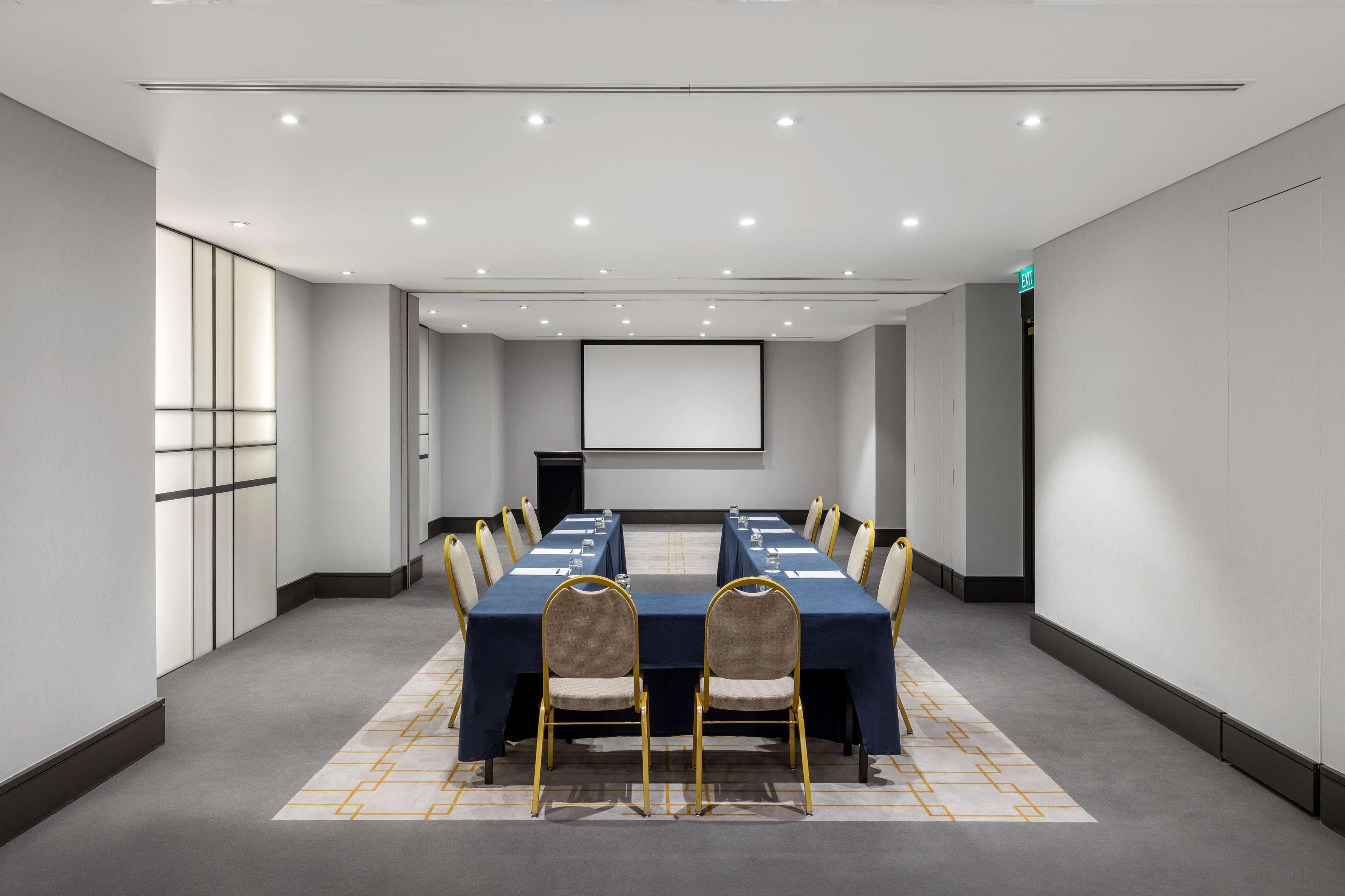 Radisson Blu Plaza Hotel ซิดนีย์ ภายนอก รูปภาพ The photo shows a modern conference room. The space is well-lit, featuring overhead lights and a neutral color palette. In the center, there is a long rectangular table covered with a navy blue tablecloth, surrounded by several chairs with beige upho