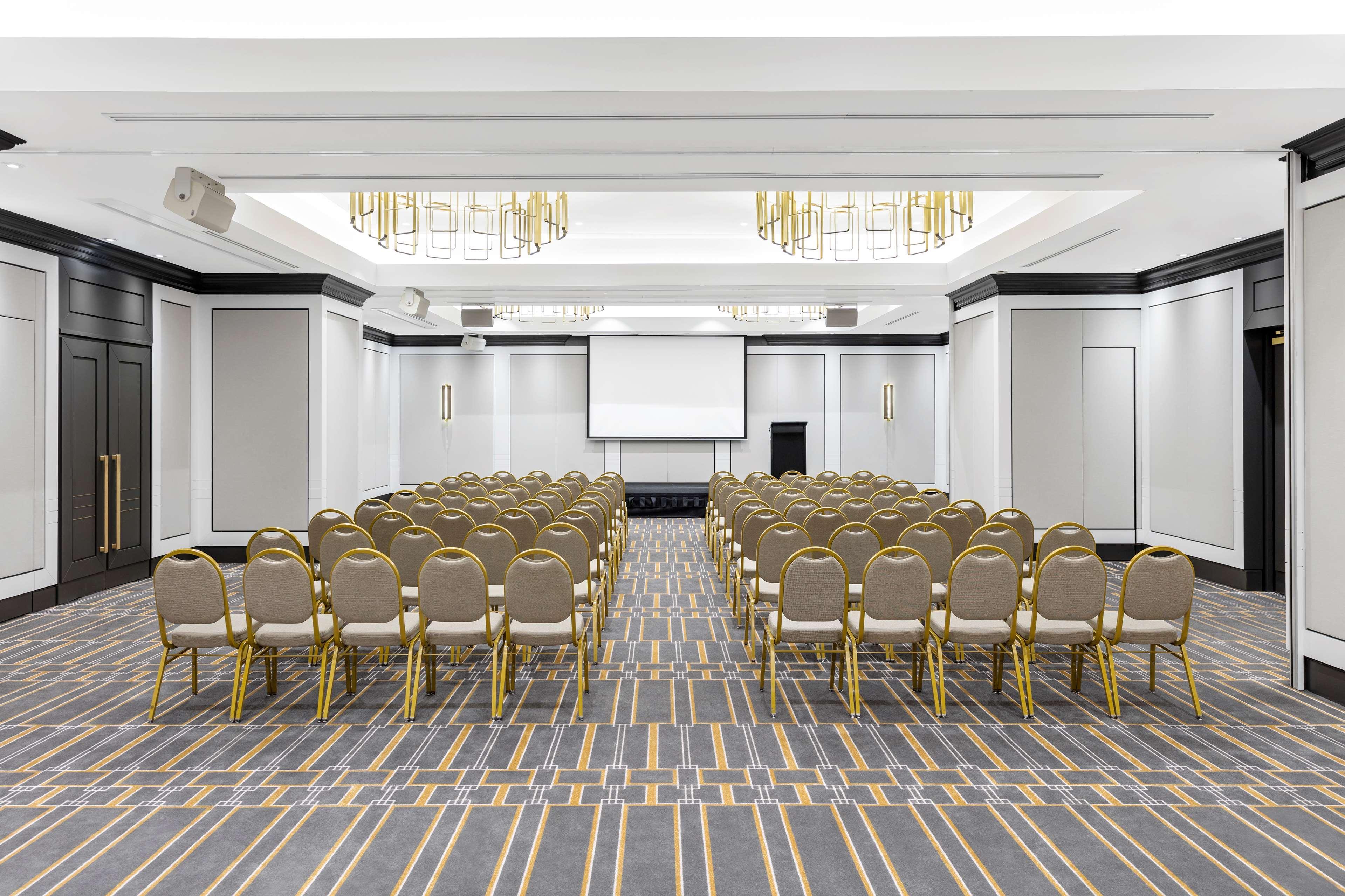 Radisson Blu Plaza Hotel ซิดนีย์ ภายนอก รูปภาพ The photo shows a spacious conference room set up for an event. There are multiple rows of beige chairs arranged in front of a screen at the front of the room. The room features modern decor, with a clean and elegant design. The ceiling has decorativ