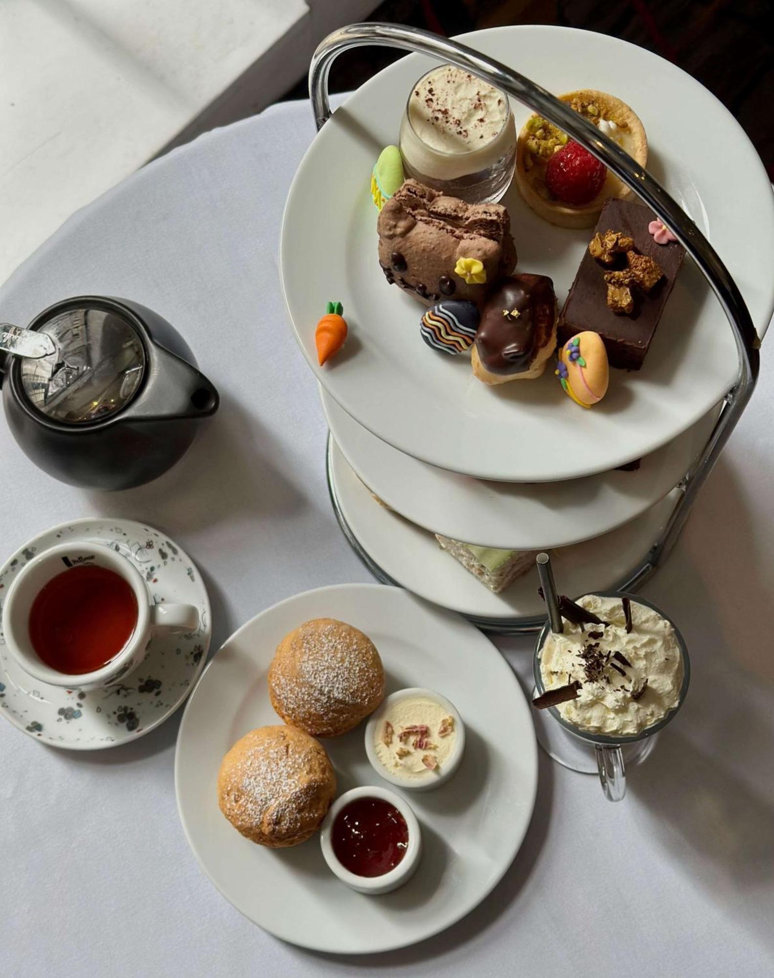 Radisson Blu Plaza Hotel ซิดนีย์ ภายนอก รูปภาพ The photo displays a delightful afternoon tea setting. There is a three-tiered stand filled with various treats, including small pastries, chocolates, and colorful desserts. A cup of tea is placed beside the stand, accompanied by a teapot. On a separ