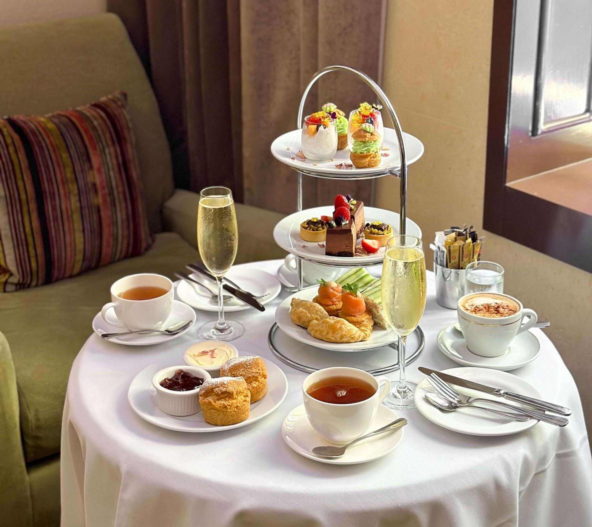 Radisson Blu Plaza Hotel ซิดนีย์ ภายนอก รูปภาพ The photo depicts a beautifully arranged table set for afternoon tea. At the center, there is a three-tiered stand filled with a variety of desserts, including small cakes, pastries, and fruit-topped treats. Surrounding the stand are cups of tea and 